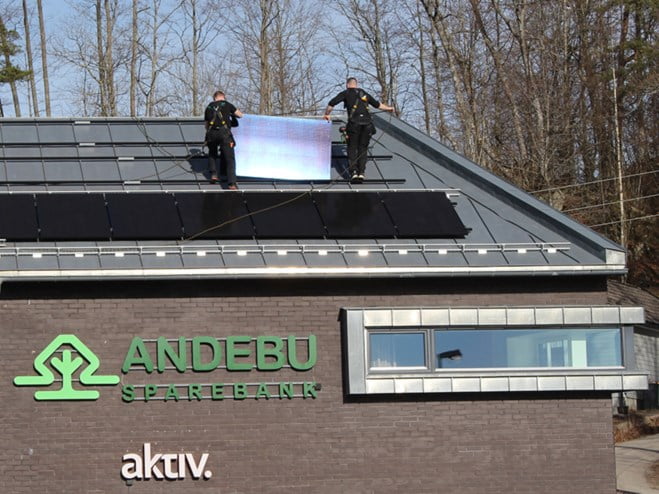 To personer monterer solpaneler på bankbygget.